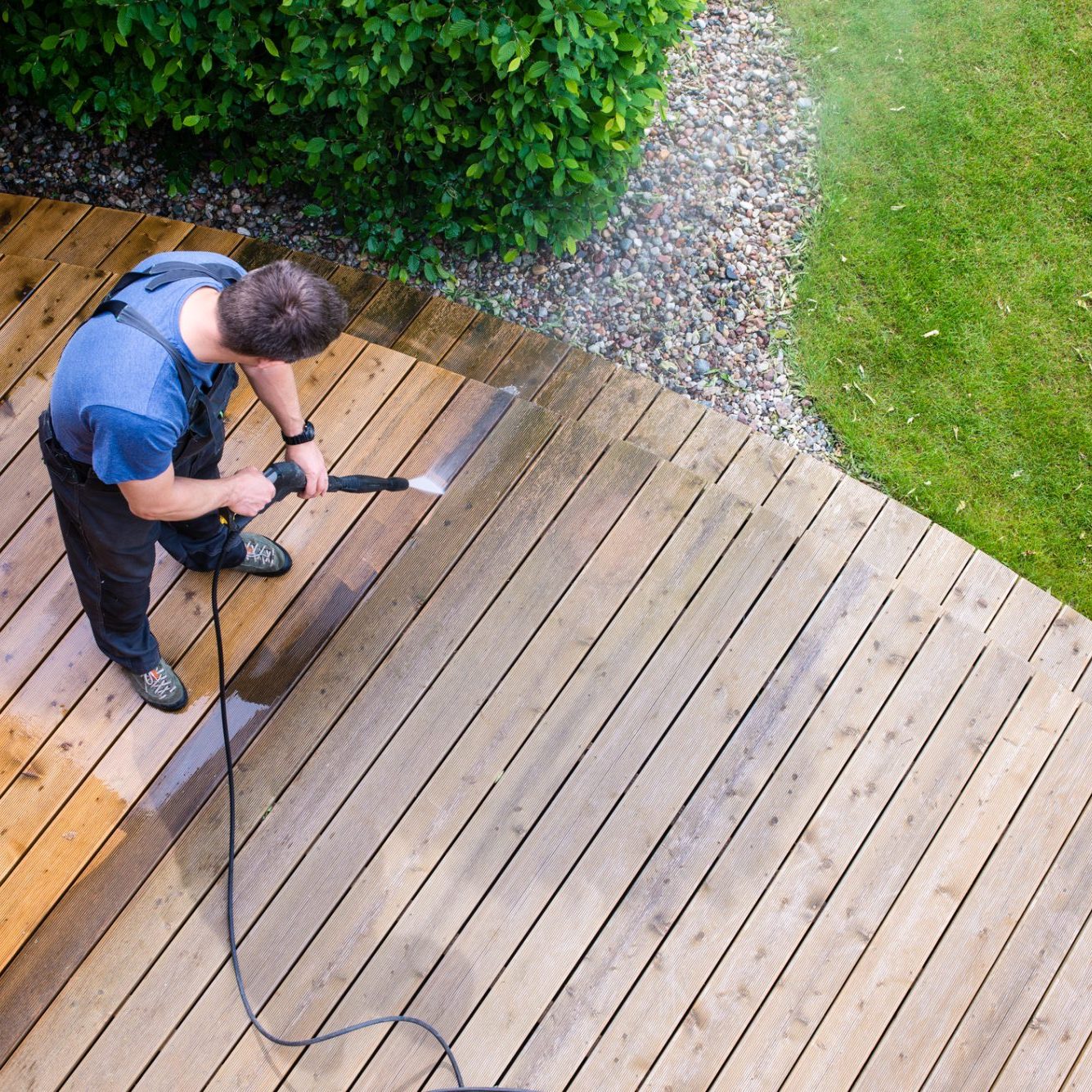 Man cleaning terrace with a power washer - high water pressure cleaner on wooden terrace surface